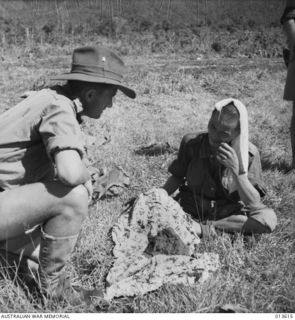 1942-11-19. NEW GUINEA. KOKODA. AN OFFICER TALKS WITH ONE OF THE FIRST JAPANESE PRISONERS CAPTURED IN THE KOKODA AREA. THE FLAG IS ONE GIVEN AT A FAREWELL PARTY BEFORE THE JAPANESE LEFT FOR ACTIVE ..