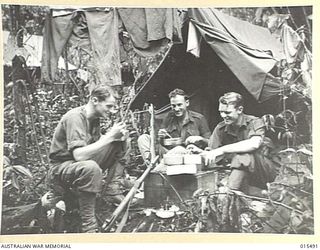 1943-08-10. NEW GUINEA. MOUNT TAMBU FIGHTING. SGT. DOUG. BAXTER OF NORTHCOTE, VIC., CAPT. RON REDUP, OF COBURG, VIC., AND SGT. ERNIE SPENCER, OF BRUNSWICK, VIC., BREAKFAST OUTSIDE THEIR TENT IN THE ..