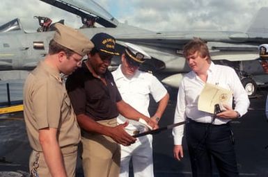 ENSIGN Quimby, public relations officer of the nuclear-powered aircraft carrier USS CARL VINSON (CVN 70), presents a photograph of the ship to country singer Charlie Pride. The entertainer is aboard the ship to film a holiday message for the Armed Forces Radio and Television Service