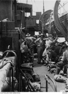 1942-12-13. TROOPS FROM THE 2/9TH BATTALION AIF AMIDSHIPS BY THE FUNNEL OF THE CORVETTE HMAS BROOME, EN ROUTE FROM MILNE BAY TO THE BUNA AREA. ROPE LADDERS ARE BEING RIGGED FOR ACCESS TO THE SHIP'S ..