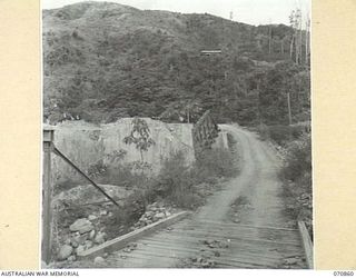 WAU - LAE ROAD, NEW GUINEA, 1944-02-20. A SECTION OF THE ROAD SHOWING THE DAMAGED CONCRETE SECTION OF THE BRIDGE