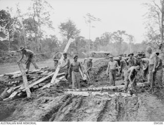 A Jeep of 2/11 Field Regiment, Royal Australian Artillery, loaded with stores for forward troops, waiting while gunners carry out running repairs replacing corduroy on a section of the Buin road ..