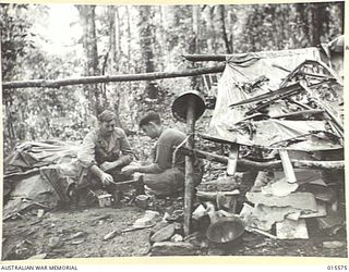 1943-08-16. NEW GUINEA. MOUNT TAMBU. SGT. WILLIAM ROOF, OF MARYVILLE, CALIFORNIA, AND SGT. WIN. BEATTY, OF PORTLAND, OREGON, PREPARING THEIR MEAL AT A CAMP THEY MADE ON MOUNT TAMBU BY STRAPPING ..