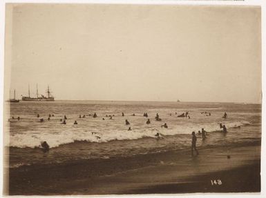 Large group swimming at the beach, with ships