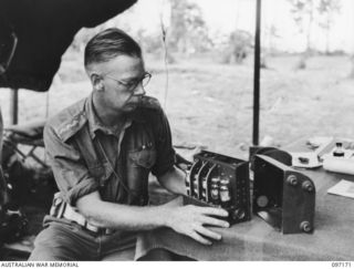 PILA PILA, RABAUL, NEW BRITAIN. 1945-09-25. CAPTAIN V.W. BAYLISS, OFFICER COMMANDING 4 INFANTRY BRIGADE SIGNAL SECTION, 11 DIVISION SIGNALS, EXAMINING A JAPANESE RADIO SET