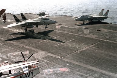 An overhead right front view of an F-14A Tomcat from Fighter Squadron 51 (VF-51) landing on the flight deck of the aircraft carrier USS KITTY HAWK (CV-63)