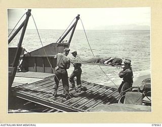 BOUGAINVILLE ISLAND, 1945-01-21. TROOPS OF THE 42ND INFANTRY BATTALION CARRYING BATTLE CASUALTIES ON TO A BARGE AT THE MAWARAKA BEACH- HEAD FOR TRANSPORT TO THE ADVANCED DRESSING STATION. ..