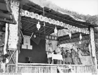 RABAUL, NEW BRITAIN. 1945-10-10. MAJOR GENERAL K.W. EATHER, GENERAL OFFICER COMMANDING 11 DIVISION, COLONEL WOO YIEN AND J. FERGUSON, INTERPRETER, ADDRESSING CHINESE TROOPS FROM A STAGE AT THE ..