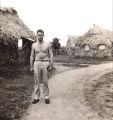 John Gunderson by thatched buildings, Fiji, 1940s