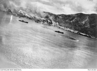 Rabaul, New Britain. 1943-11-02. Aerial photograph of shipping in the harbour. In the background smoke envelops the town which is on fire during an air attack by seventy-five Mitchell aircraft ..
