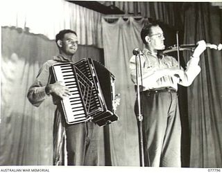 LAE BASE AREA, NEW GUINEA. 1944-12-27. VX147374 LANCE CORPORAL ALLAN TRICKEY, PIANO ACCORDIONIST (1) AND VX29583 CHAPLAIN G.G. PAYNE, VIOLIN (2) RENDERING AN ITEM DURING THE CHRISTMAS CONCERT ..