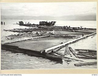 LAE, NEW GUINEA. 1944-06-09. THE REMAINS OF THE WHARF WHICH COLLAPSED AT 0930 HOURS ON 1944-06-09. ONE OF THE BARGES SALVAGING DEBRIS IS SEEN WORKING ALONGSIDE THE FLOATING TIMBER