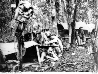1943-08-16. NEW GUINEA. MOUNT TAMBU. LIVING QUARTERS MADE OF GROUND SHEETS SUSPENDED ON PIECES OF TIMBER AT AN AMERICAN ARTILLERY BATTERY IN THE HEART OF THE JUNGLE. WRITING HOME UNDER DIFFICULTIES ..