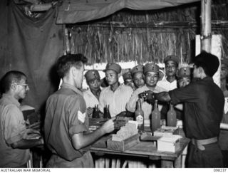 KARAVIA BAY, NEW BRITAIN. 1945-10-24. SERGEANT W. GORDON, WORKING UNDER THE DIRECTION OF THE RED CROSS, AND ASSISTED BY TIM MACK, A CHINESE CIVILIAN INTERPRETER, DISTRIBUTE GOODS TO THE AMOUNT OF ..