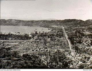 Rabaul, New Britain, 1945-10. Elevated view from a hillside, showing Simpson Harbour (left) and the road known as Malungai Avenue stretching away to low hills in the distance
