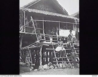 PORT MORESBY, PAPUA. 1932-09-17. NATIVE WOMEN AND CHILDREN POSE IN FRONT OF THEIR HOUSE BUILT ON STILTS, NOTE THE BICYCLE ON THE VERANDA. (NAVAL HISTORICAL COLLECTION)