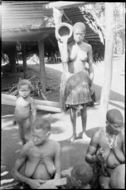 Two women working on pots in the foreground and a woman with a pot on her shoulder behind, Madang, New Guinea, 1935 / Sarah Chinnery