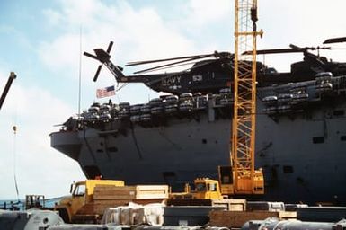 Equipment and supplies are loaded aboard the amphibious assault ship USS GUAM (LPH 9) prior to its departure to the Persian Gulf. A Helicopter Mine Countermeasures Squadron 14 (HM-14) RH-53D from the Sea Stallion helicopter is parked on the flight deck