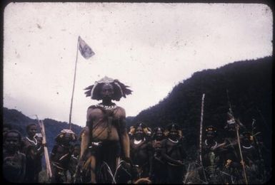 Papuan tribesman standing in front of the Australian flag flying for the first time in the Lavani Valley, Papua New Guinea, 1955 / Albert Speer