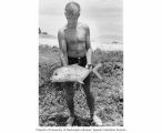 Arthur D. Welander holding a fish specimen collected for radioanalysis from a pool on Enjebi Island, summer 1964