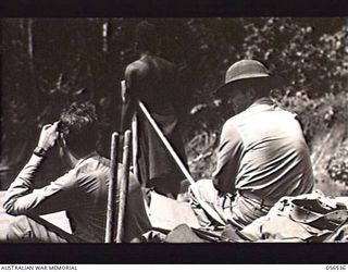 TAVERI RIVER, NEW GUINEA, 1943-09-05. TWO MEMBERS OF THE UNITED STATES ARMY SEATED IN THE BOWS OF A BARGE. NATIVE IN THE BACKGROUND IS THE LOOKOUT FOR SNAGS, SANDBARS AND CROCODILES