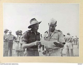 JACQUINOT BAY, NEW BRITAIN, 1945-08-23. WING COMMANDER P.A. MATHESON, ROYAL NEW ZEALAND AIR FORCE (2) LISTENING TO ADVICE ON HOW TO PICK WINNERS DURING THE VICTORY CUP RACE MEETING HELD ON THE ..