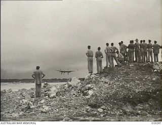 VIVIGANI, GOODENOUGH ISLAND, PAPUA. C. 1943-12-21. BEAUFIGHTER PILOTS OF NO. 30 SQUADRON RAAF WATCH AMERICAN LIGHTNING FIGHTER AIRCRAFT LAND ON RETURN FROM FIGHTER COVER WORK, SOME OF THEM ..