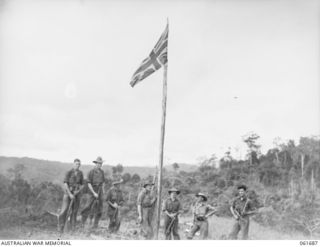 WAREO, NEW GUINEA. 1943-12-09. GROUP OF OFFICERS AND MEN OF THE 2/23RD AUSTRALIAN INFANTRY BATTALION, GROUPED AROUND THE UNIT VICTORY FLAG. THIS FLAG WAS PREVIOUSLY RAISED OVER KOKODA, BUNA AND ..