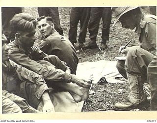 DUMPU, RAMU VALLEY, NEW GUINEA, 1944-02-10. SX15733 CAPTAIN M.G. GRATTON, REGIMENTAL MEDICAL OFFICER (1), 57/60TH INFANTRY BATTALION, 15TH INFANTRY BRIGADE, INSPECTING THE FEET OF V155861 PRIVATE ..