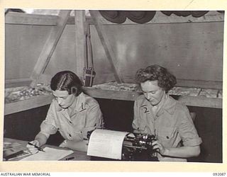 LAE, NEW GUINEA, 1945-05-21. SERGEANT J. GRIEVE, ORDERLY ROOM SERGEANT (1), DICTATING A REPORT TO PRIVATE R.F. GOULD (2) IN THE ORDERLY ROOM AT THE AUSTRALIAN WOMEN'S ARMY SERVICE BARRACKS IN ..