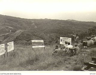 FINSCHHAFEN AREA, NEW GUINEA, 1944-03-17. VX5104 MAJOR V.J. SCHOFIELD, GENERAL STAFF OFFICER II, LIAISON OFFICER OF THE 2ND AUSTRALIAN CORPS POINTS OUT FEATURES OF TERRAIN TO OBSERVERS ON ..