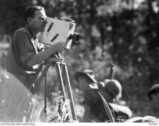 KOKODA TRAIL, NEW GUINEA. 1943-12-19. MR GEORGE HEATH, CHIEF CAMERAMAN OF CHAUVEL'S PRODUCTIONS, TAKING A SCENE FOR THE PRODUCTION, "RATS OF TOBRUK"