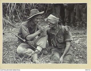 DAGUA, NEW GUINEA. 1945-03-27. PRIVATE R.E. BYERS, 2/2 INFANTRY BATTALION (1), GIVES A LIGHT TO LANCE-CORPORAL A.B. DAWSON (2), WHO WAS WOUNDED WHEN A JAPANESE THREW A GRENADE AT CLOSE RANGE