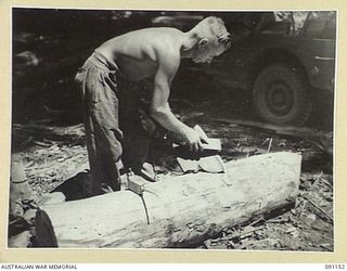 BANAK, AITAPE-WEWAK SECTOR, NEW GUINEA. 1945-04-21. SAPPER E.A. LOVE, 2/1 FIELD COMPANY, ROYAL AUSTRALIAN ENGINEERS, SHARPENING A BROAD AXE USED FOR SQUARING TIMBER FOR THE CONSTRUCTION OF URGENTLY ..