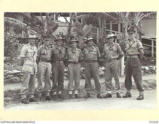 PORT MORESBY, NEW GUINEA. 1944-05-31. OFFICERS OF THE NEW GUINEA DETAILS DEPOT OUTSIDE THE STAFF OFFICERS' MESS, (LEFT BACKGROUND). THE BUILDING WITH THE RAMP (RIGHT BACKGROUND) FORMED THE ..