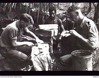 FARIA VALLEY, NEW GUINEA. 1943-10-22. SX18032 PRIVATE (PTE) L. HADE (LEFT) AND SX17729 PTE L. A. J. HARDING OF THE 2/27TH AUSTRALIAN INFANTRY BATTALION, CUTTING AND SPREADING FRESH BREAD FOR THE ..