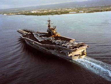 An aerial stern view of the US Navy (USN) Forrestal Class Aircraft Carrier USS RANGER (CV 61), with her Sailors manning the rails and aircraft of the Carrier Air Wing 2 (CVW-2) on her deck, as she arrives at Pearl Harbor Naval Base in Pearl Harbor, Hawaii (HI). In the background is Ford Island