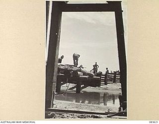 ANAMO AREA, NEW GUINEA. 1944-11-23. 2/2 FIELD COMPANY, ROYAL AUSTRALIAN ENGINEERS, TROOPS VIEWED THROUGH A PILE DRIVER, SHOWING PROGRESS MADE IN 6 DAYS DURING BRIDGE CONSTRUCTION AT AN UNNAMED ..