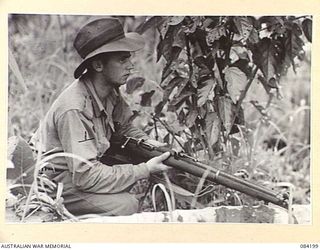 SUAIN PLANTATION, NEW GUINEA. 1944-12-10. PRIVATE F.L. BOYLE, 2/4TH INFANTRY BATTALION, STANDS GUARD BEHIND A SMALL BUSH AS MAJOR-GENERAL J.E.S. STEVENS, GENERAL OFFICER COMMANDING 6 DIVISION, ..