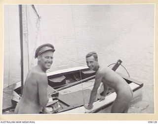 CAPE WOM, NEW GUINEA. 1945-10-20. CAPTAIN J.V. WILKINSON (1) AND CAPTAIN C.,W. YOUNG (2), OFFICERS OF 6 DIVISION LOADING FRUIT AND WATER INTO THEIR 12 FOOT SKIFF BEFORE LEAVING ON A 15 MILE VOYAGE ..