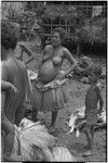 Mortuary ceremony: pregnant woman wearing long fiber skirt, next to piles of fiber skirts and banana leaf bundles (wealth items)