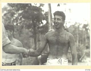 LAE, NEW GUINEA. 1944-06-08. NX115243 CRAFTSMAN P. MANKEY (1), WINNER OF THE NOVELTY FLAG EVENT, AND COVERED IN BLACK DUST, IS CONGRATULATED BY A MEMBER OF THE 2/7TH ADVANCED WORKSHOP AT THEIR ..