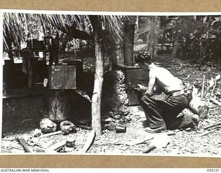 DUMPU, NEW GUINEA, 1943-10-23. NX6198 PRIVATE G. NEW, COOK OF HEADQUARTERS, 7TH AUSTRALIAN DIVISION AREA COOKING A BATCH OF SCONES IN THE UNIT'S OUTDOOR BUILT-IN OVEN WITH OIL AND WATER DRIP BURNER