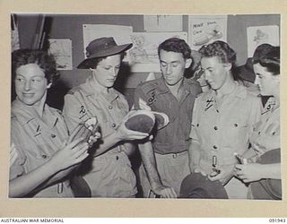 LAE, NEW GUINEA, 1945-05-18. PERSONNEL FROM THE AUSTRALIAN WOMEN'S ARMY SERVICE BARRACKS, TAKING PART IN A CONDUCTED TOUR ARRANGED BY ARMY AMENITIES SERVICE, BEING SHOWN SAMPLES OF SLIPPERS MADE BY ..