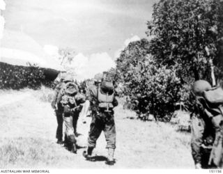 New Guinea. November 1942. US troops in battle gear advance towards the Japanese at Buna. In the background is a native church with thatched roof