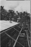 House-building: men frame a building and attach corrugated metal roofing