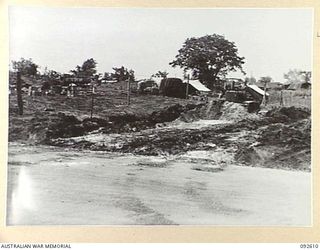 CAPE WOM, NEW GUINEA. 1945-05-29. A GENERAL VIEW OF THE ASSISTANT DIRECTOR OF ORDNANCE SERVICE SECTION OF FIELD MAINTENANCE CENTRE, WITH A BULLDOZER WORKING AT ITS ENTRANCE, DURING EARLY STAGES OF ..