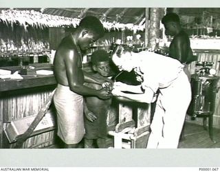 THE SOLOMON ISLANDS, 1945-03-24. AN AUSTRALIAN PATHOLOGIST AT WORK WITH NATIVE ISLANDERS. (RNZAF OFFICIAL PHOTOGRAPH.)