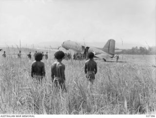 WANIGELA, NEW GUINEA. 1942-10. PAPUAN NATIVES WATCHING THE UNLOADING OF TROOPS OF THE 3RD BATTALION, 128TH REGIMENT, 32ND U.S. DIVISION BEING FLOWN IN FROM PORT MORESBY. tHE AIRCRAFT IN THE ..