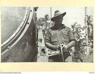 SOUTH ALEXISHAFEN, NEW GUINEA. 1944-07-24. SX10975 WARRANT OFFICER II, R. FENNELL, BATTERY SERGEANT MAJOR, NO. 27 BATTERY, 2/14TH FIELD REGIMENT STANDS BESIDE A CAPTURED JAPANESE SEARCHLIGHT